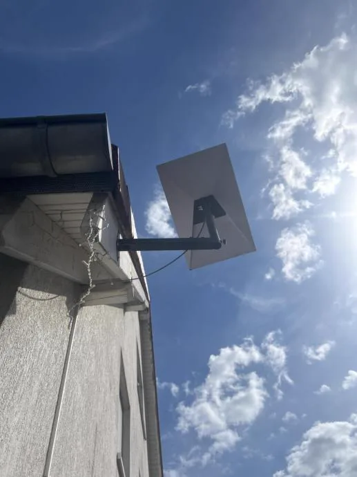 Starlink antena na teleskopskom nosaču ispod oluka, krak odmaknut od fasade prema nebu